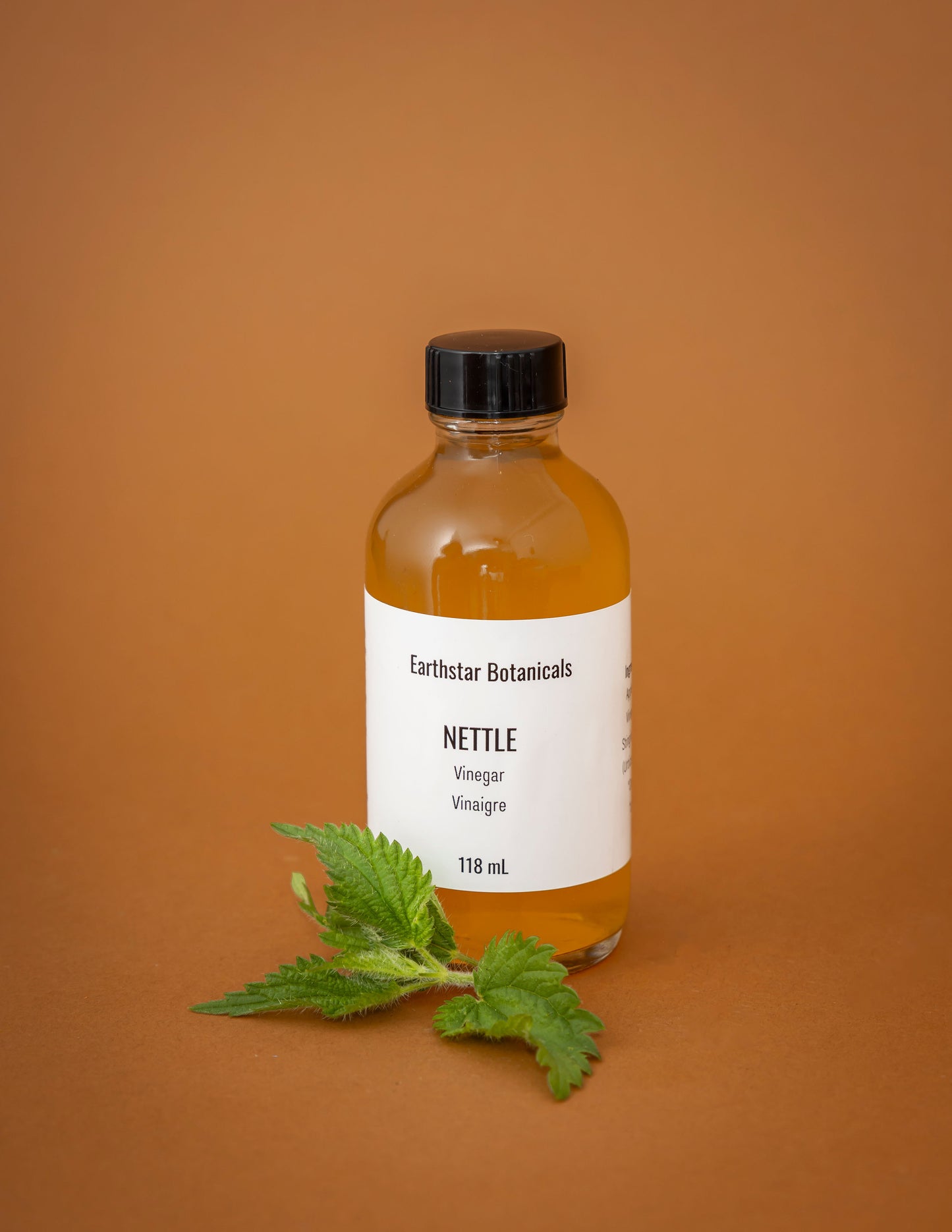 Bottle of Earthstar Botanicals Nettle Vinegar on an orange background