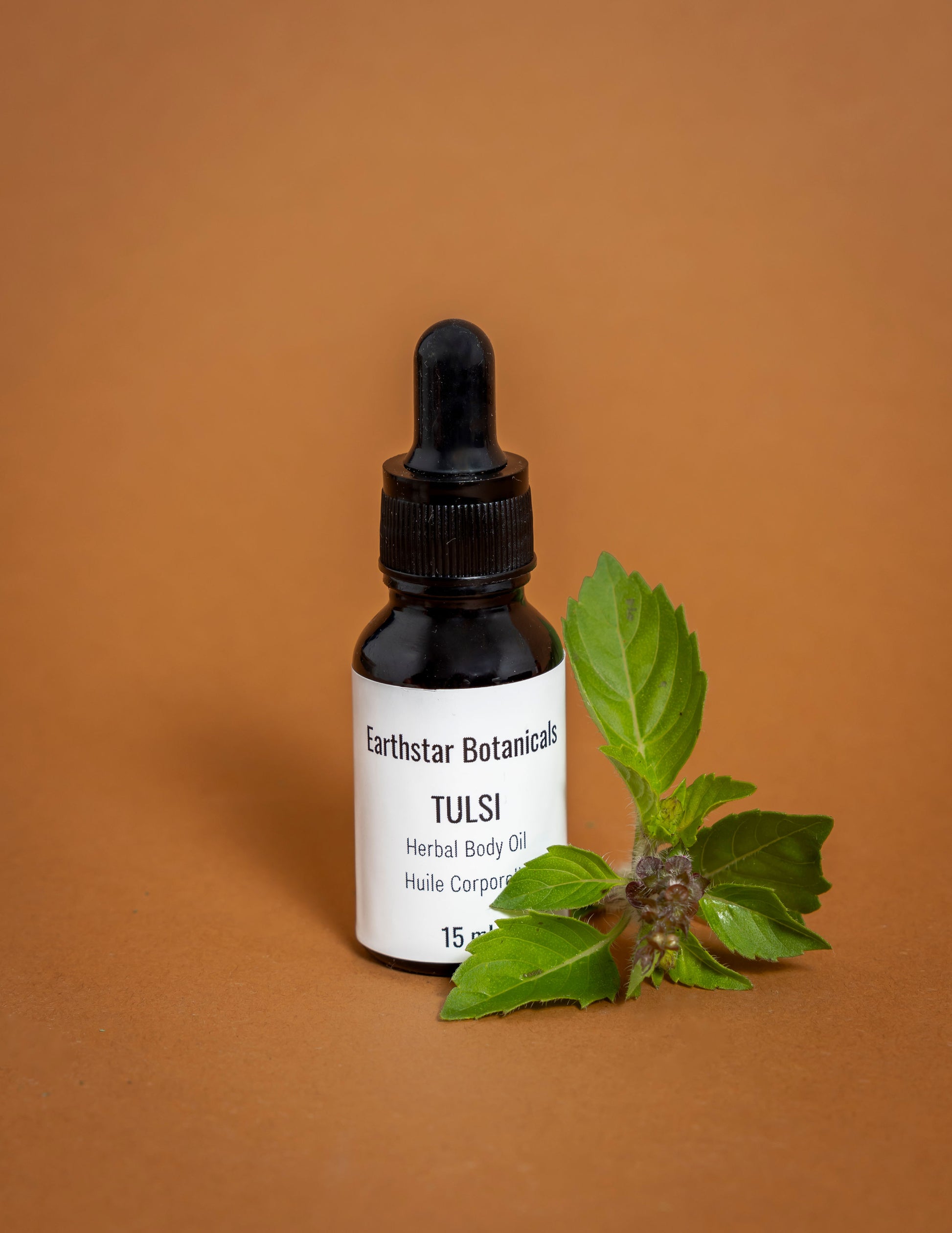 Bottle of Earthstar Botanicals Tulsi Herbal Body Oil with a dropper on an orange background