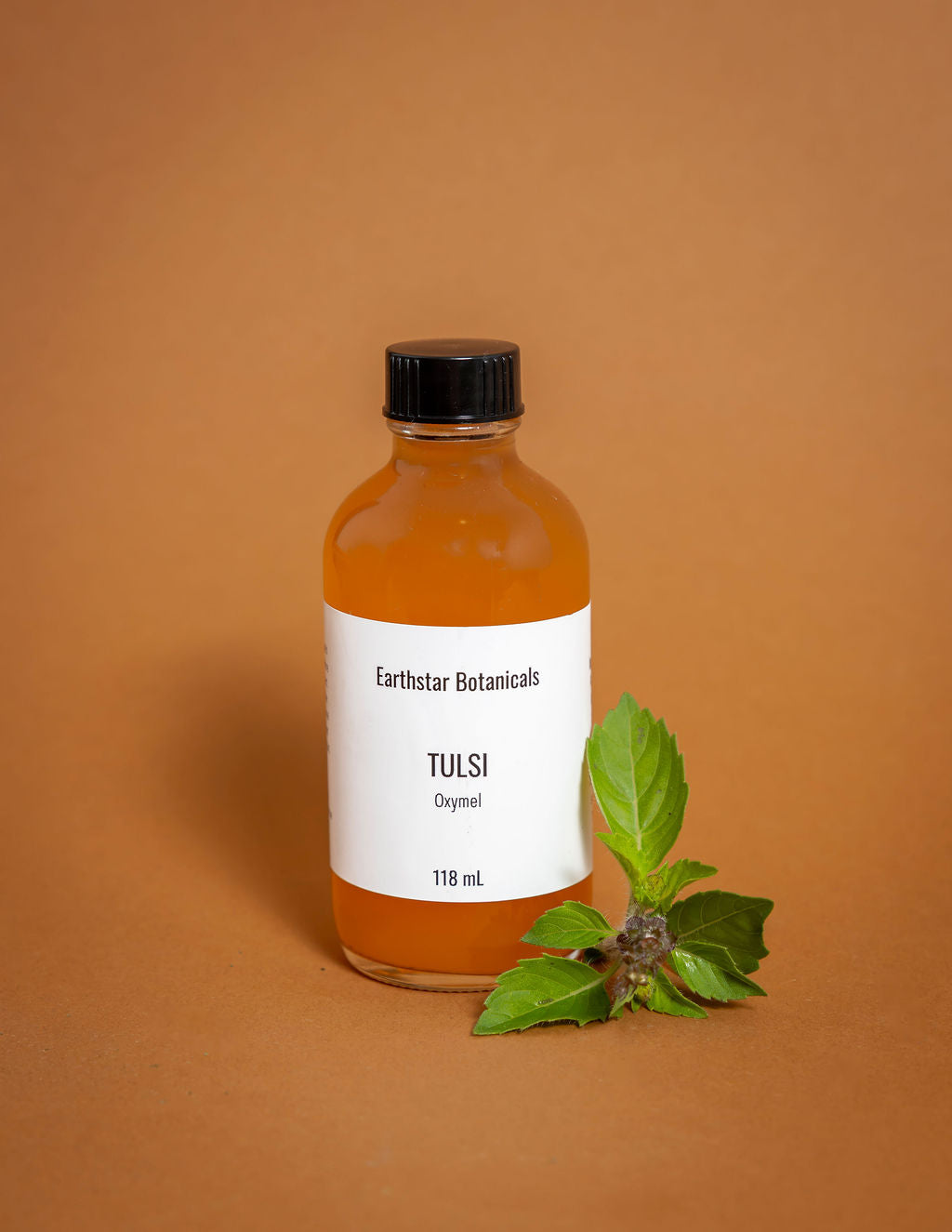 Bottle of Earthstar Botanicals Tulsi tincture with a leaf on an orange background