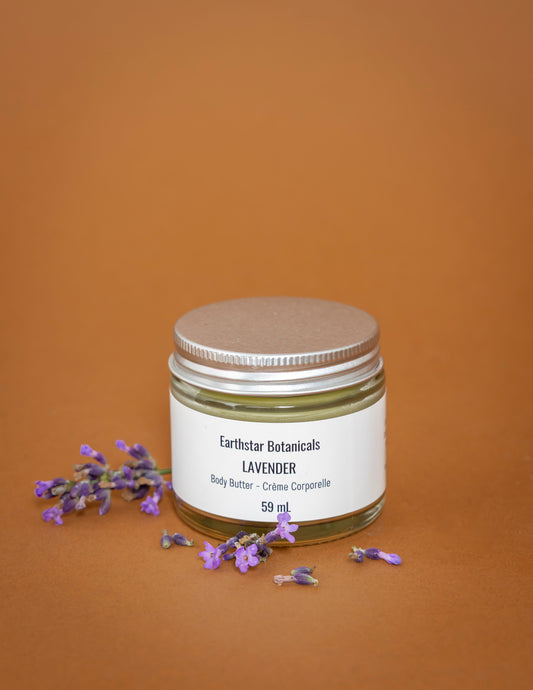 Jar of Earthstar Botanicals Lavender Body Butter surrounded by Lavender blossoms on an orange background