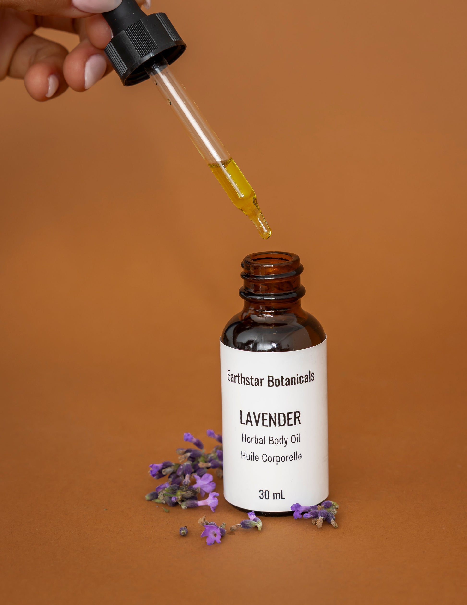 Bottle of Earthstar Botanicals Lavender Herbal Body Oil with a dropper on an orange background