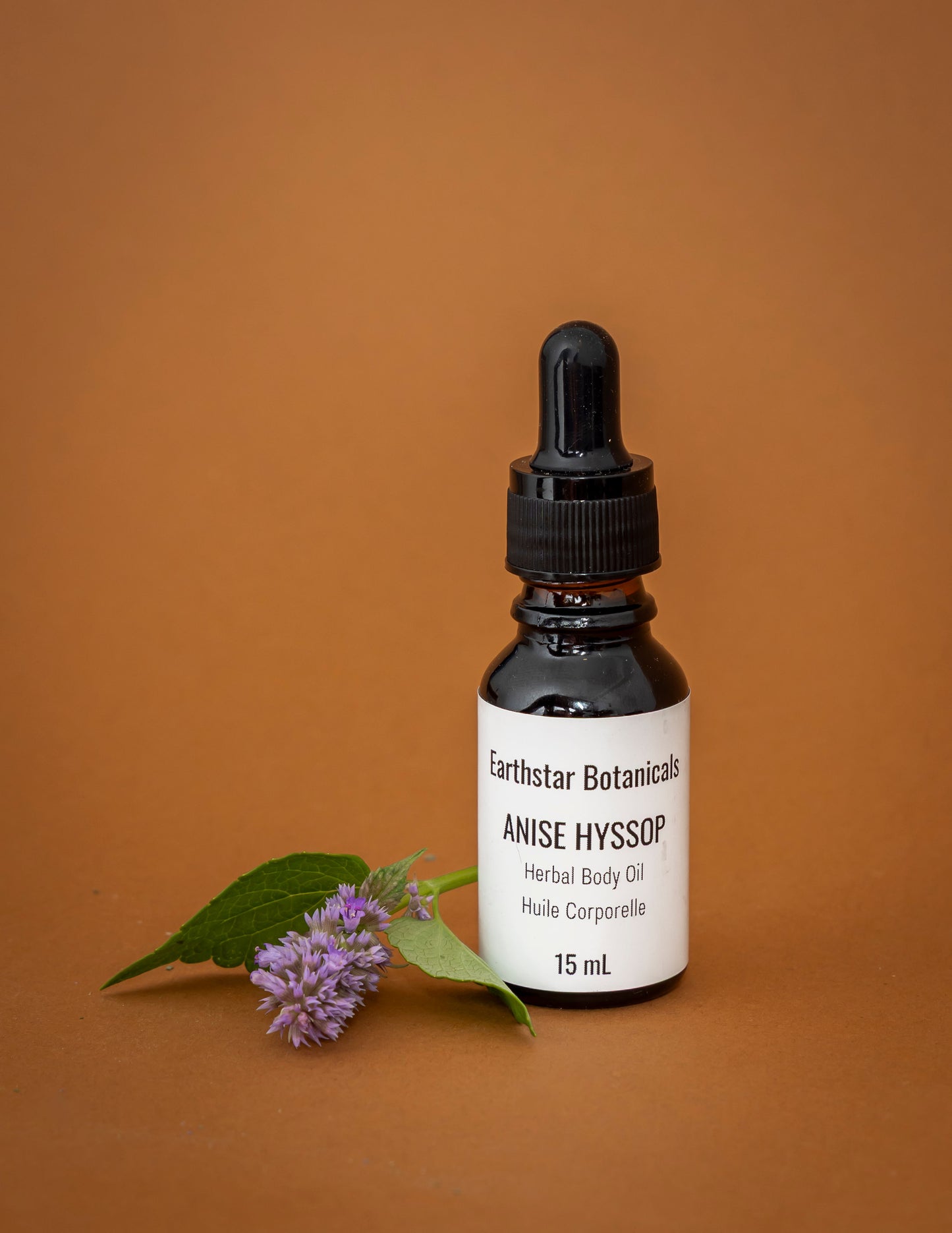 Bottle of Earthstar Botanicals Anise Hyssop Herbal Body Oil on an orange background